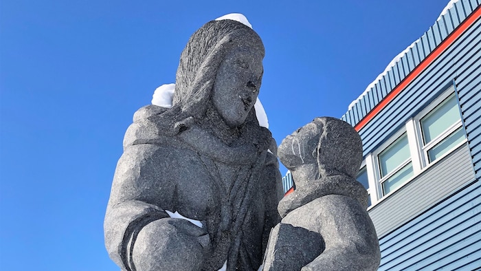 Une sculpture en granit devant un bâtiment, qui représente une femme et un enfant avec un livre à la main.