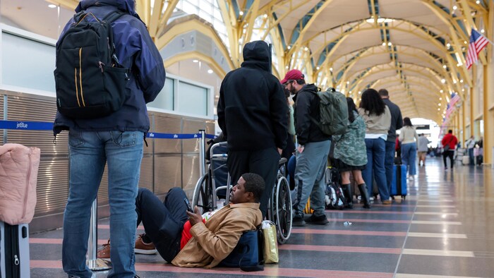 Des voyageurs attendent aux contrôles de sécurité d'un aéroport.