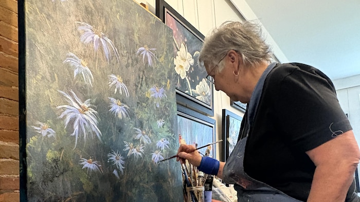 Diane est à droite de l’image. Elle peint un aster à feuilles de linaire sur une grande toile dans son atelier.