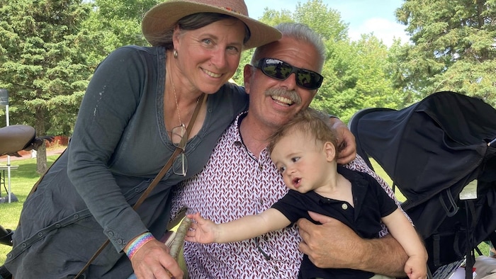 Deux grands-parents et un jeune enfant pose pour une photo. L'enfant est de profile car il est davantage intéressé par l'arc artisanal que tient sa grand-mère dans ses mains.
