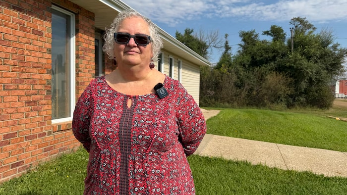 Dianne Hahn se tient debout devant une bâtisse en briques qui semble être un établissement, l'air sérieux face à la caméra.