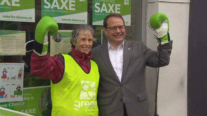 Dianne Saxe et Mike Schreiner brandissent un gant de boxe vert devant le local de campagne de Mme Saxe.