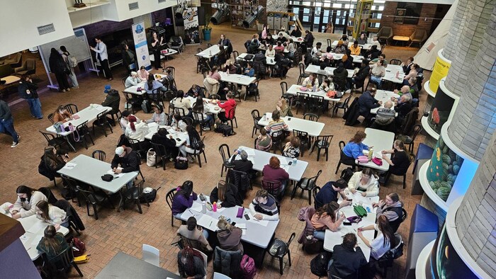 Les participants sont répartis sur des tables dans le hall du Cégep.