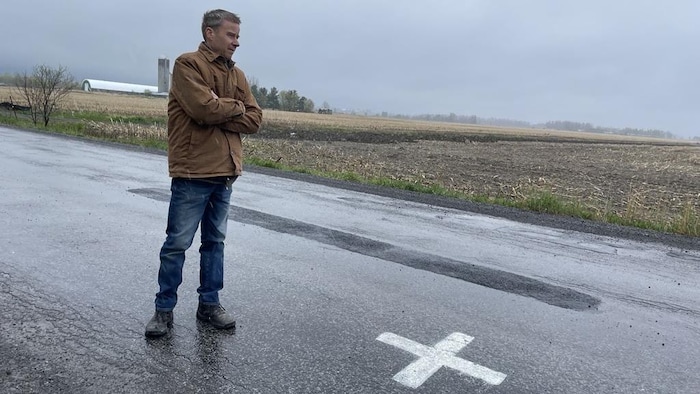 Un homme est en plein milieu d'une route avec un X peint en blanc devant lui. 