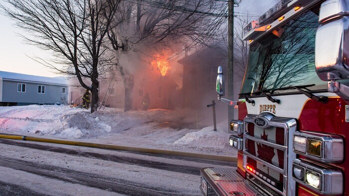 Un camion d'incendie devant une maison en flammes.