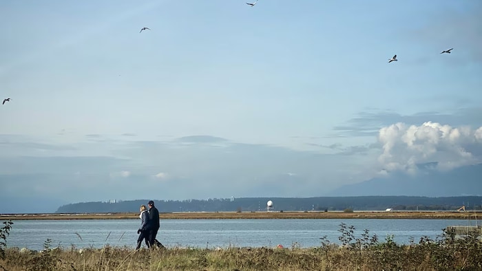 Deux personnes marchent au bord de l'eau.