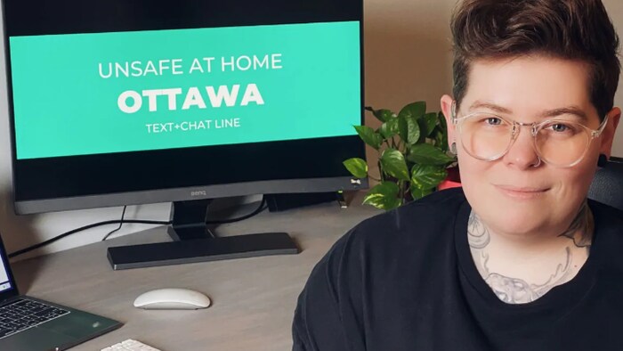 Dillon Black pose devant un ordinateur. Sur l'écran, on peut lire "unsafe at home Ottawa, text + chat line".