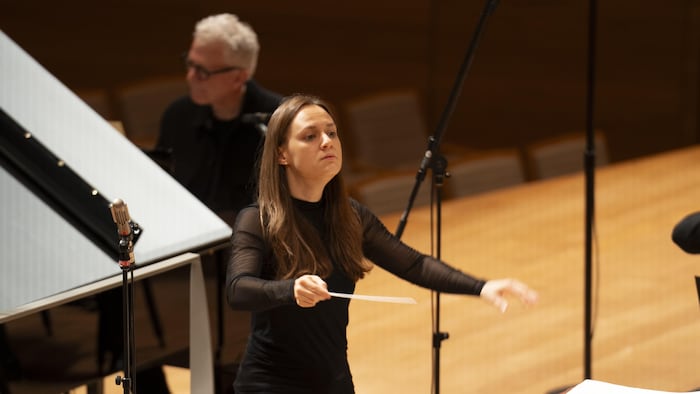 Dina Gilbert, debout sur un podium avec une baguette, dirige des musiciens
