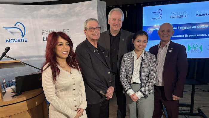 Quatre personnes posent en souriant à la caméra devant un lutrin et un écran.