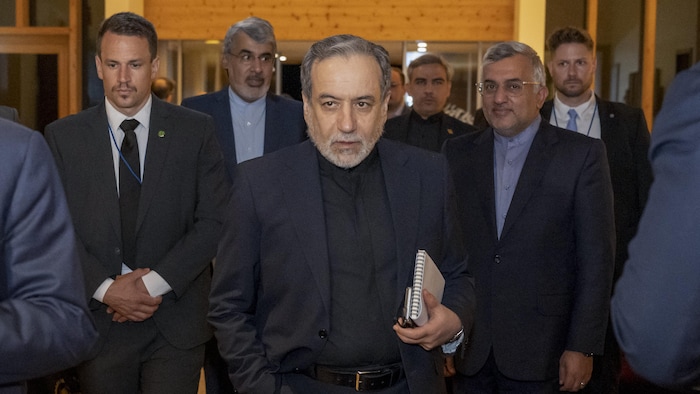 Seyyed Abbas Araghchi, calepin à la main, marche dans un corridor entouré de plusieurs personnes de son entourage.