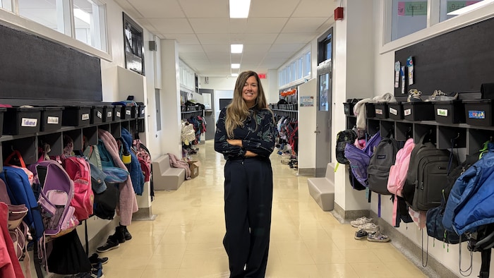 Une femme se tient au centre du corridor d'une école primaire les bras croisées.