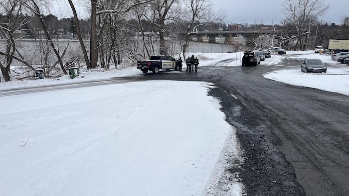 Un véhicule de police et des policiers sur une route près d'une rivière.