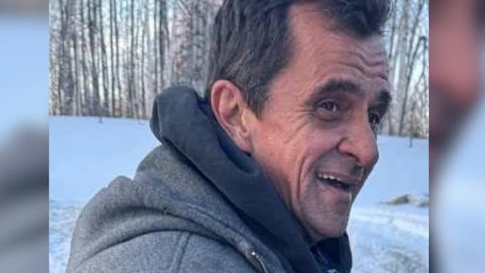 Joël Girouard sourit près d'une forêt.
