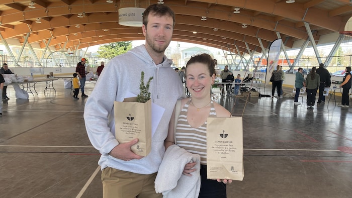 Un couple, sacs de plants d'arbres en mains, posent pour la caméra en souriant.