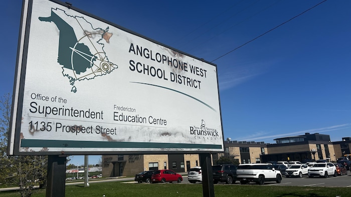 Une affiche représentant le nom du district en avant-plan, un établissement et des véhicules stationnés en arrière-plan.