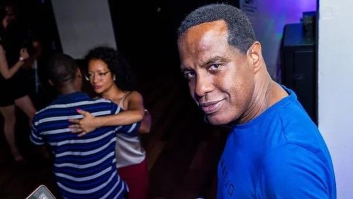 Un homme derrière une console de DJ et un ordinateur, devant une salle où un couple danse.