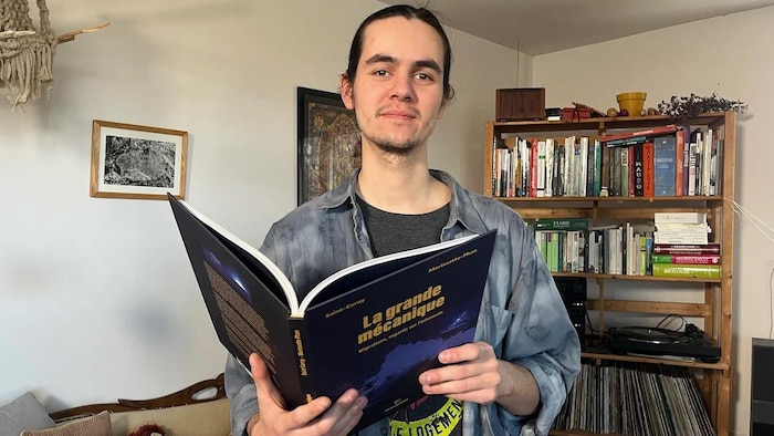 Un homme tient une bande-dessinée ouverte dans ses mains. Il sourit en regardant la caméra.