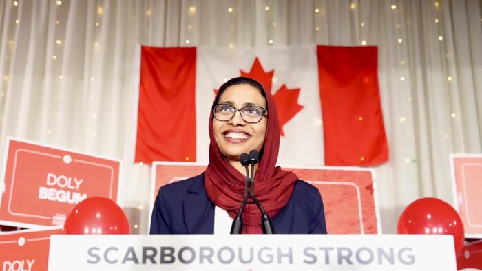Doly Begum devant un drapeau du Canada lors de son discours de victoire le 13 avril 2026.