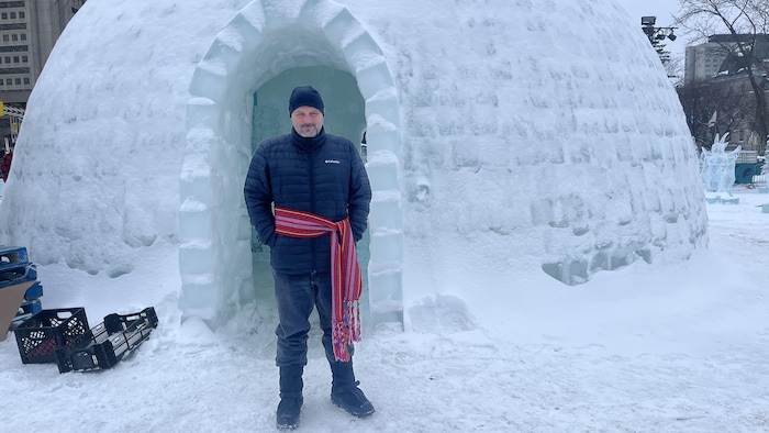 Un homme pose devant l'entrée d'un igloo. 