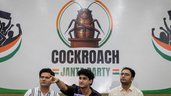 Les porte-parole du « parti des cafards », Vijeta Dahiya, Saurav Das et Ashutosh Ranka, participent à une conférence de presse, devant leur logo, qui comporte un cafard aux pattes croisées.