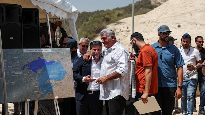 Le ministre israélien des Finances, Bezalel Smotrich, discute avec un homme, le jour d'une conférence de presse sur l'expansion des colonies pour la colonie E1, qui séparerait Jérusalem-Est de la Cisjordanie occupée, près de la colonie israélienne de Maale Adumim, en Cisjordanie occupée par Israël, le 14 août 2025.
