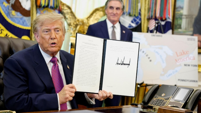 Donald Trump présente un document signé dans un bureau.