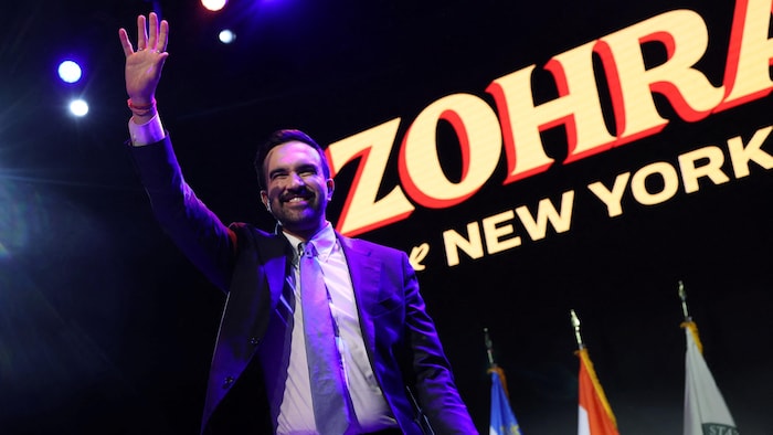 Il sourit et fait un salut de la main droite.