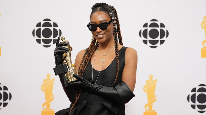 Une femme en robe noire et verres fumés pose avec un trophée.