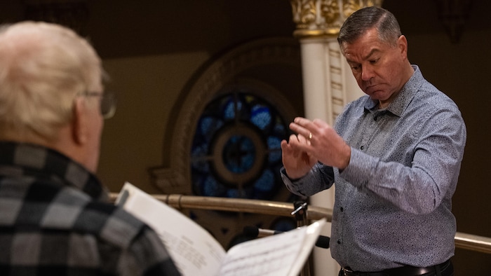 Un homme bouge les bras et les mains devant un choriste.