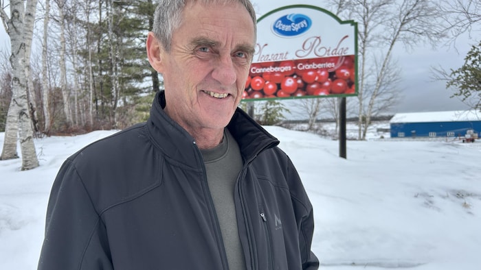 Donald Daigle pose pour la photo devant une affiche de la ferme Oceanspray Pleasant Ridge.