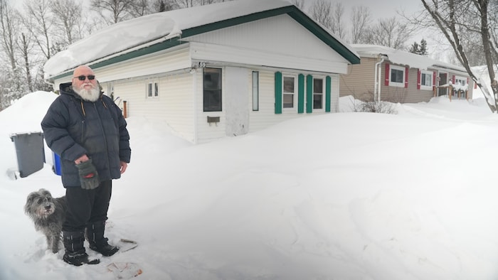 Donald Shea et son chien se tiennent devant leur maison mobile.