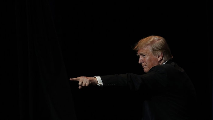 Donald Trump pointe du doigt une foule lors d'un rassemblement devant un fond noir.