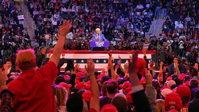 Donald Trump sur une scène, entouré de partisans qui lèvent la main.
