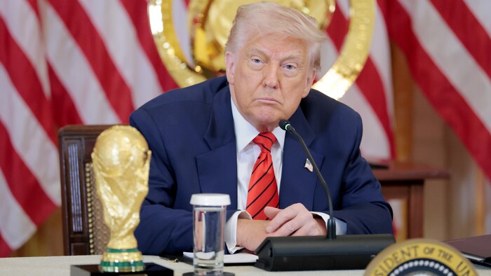 Donald Trump assis derrière un bureau sur lequel se tient la Coupe du Monde 2026. 