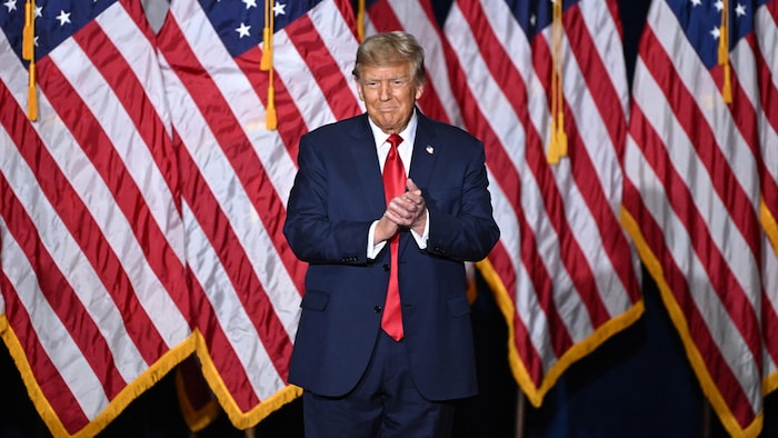 Donald Trump applaudit devant des drapeaux américains.