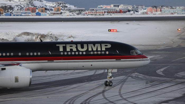 Un avion sur lequel est écrit « Trump » est posé devant un paysage de neige et de maisons.
