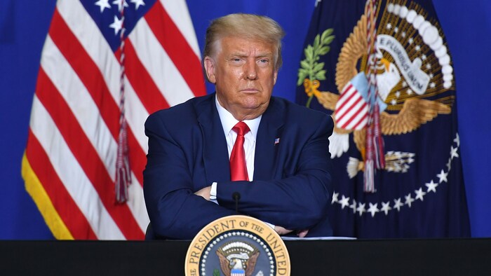 Le président, les sourcils froncés, les bras croisés, est assis.