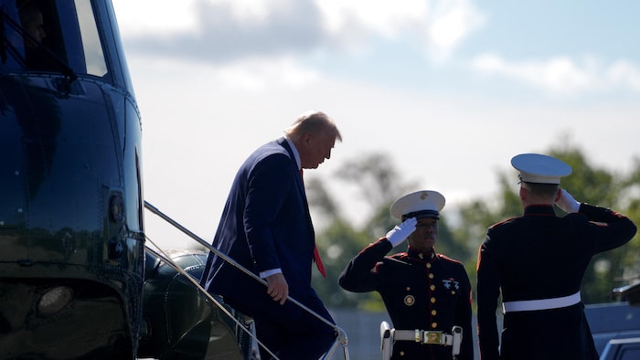 Donald Trump descend l'escalier d'un hélicoptère militaire tandis que deux soldats en uniforme le saluent.
