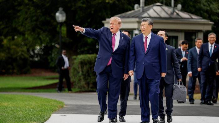 Donald Trump montre quelque chose du doigt en marchant aux côtés de Xi Jinping sur une allée.