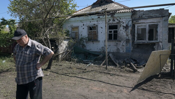 Un homme, devant une maison endommagée par un bombardement, regarde par terre.