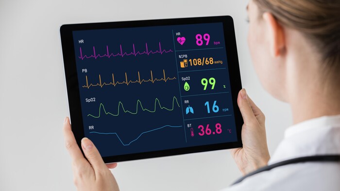 Une femme tient une tablette sur laquelle on peut voir des données médicales comme le rythme cardiaque.