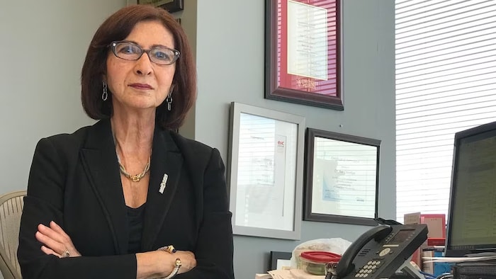 Une femme habillée en complet dans un bureau a les bras croisés.