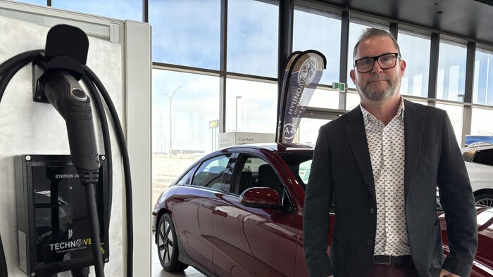 Un homme en veston prend la pose dans un concessionnaire automobile.
