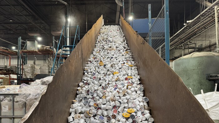 Des centaines de dosettes de café sont entreposées sur la rampe d’une machine qui va ensuite séparer le plastique du papier, à Calgary, le 2 décembre 2025.