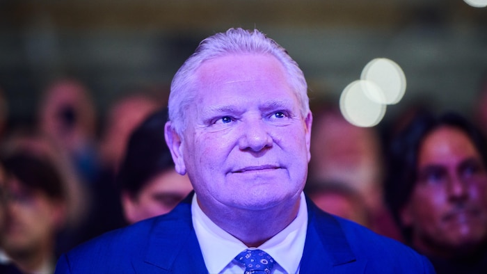 Doug Ford regarde devant lui, baigné d’une lumière bleue ambiante.