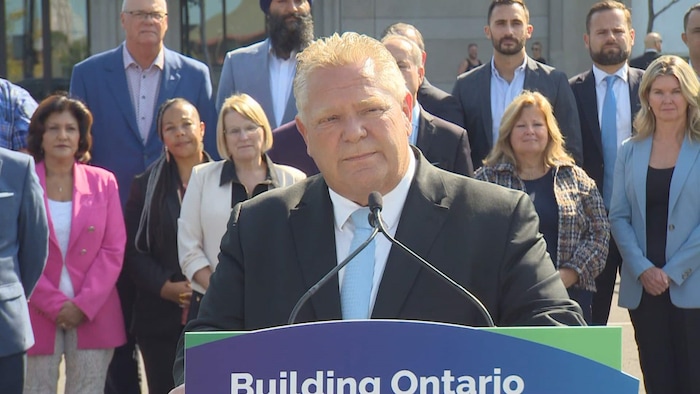 Doug Ford debout sur un podium devant les ministres ontariens.