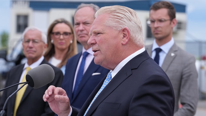 Doug Ford répond à des questions des journalistes devant des représentants de son gouvernement sur un chantier de Hamilton le 24 août 2026.
