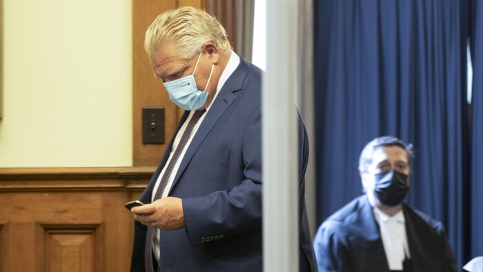Le premier ministre Doug Ford consulte son téléphone en sortant de la Chambre.