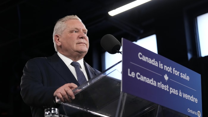 Doug Ford s'adresse aux médias. Il est à un podium qui porte une affiche disant « Le Canada n'est pas à vendre ».