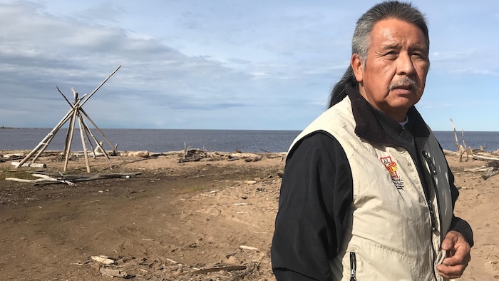 Un homme pose devant la caméra sur le bord d'une étendue d'eau à l'extérieur.